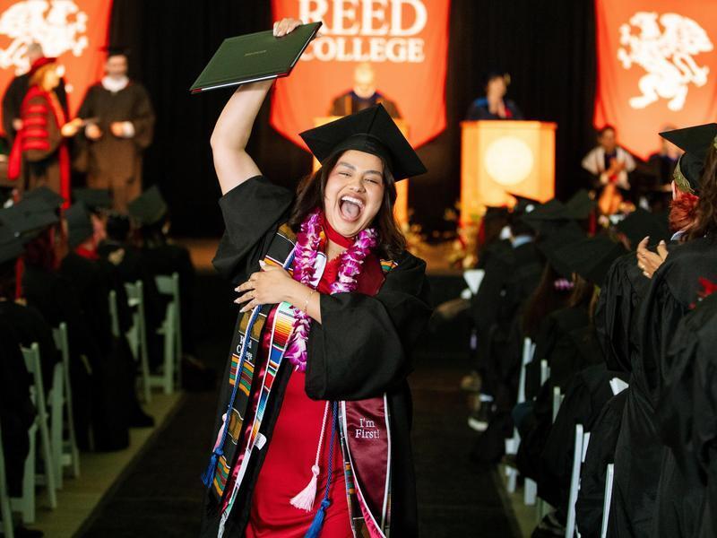 A graduate in regalia cheering with her diploma during Commencement.