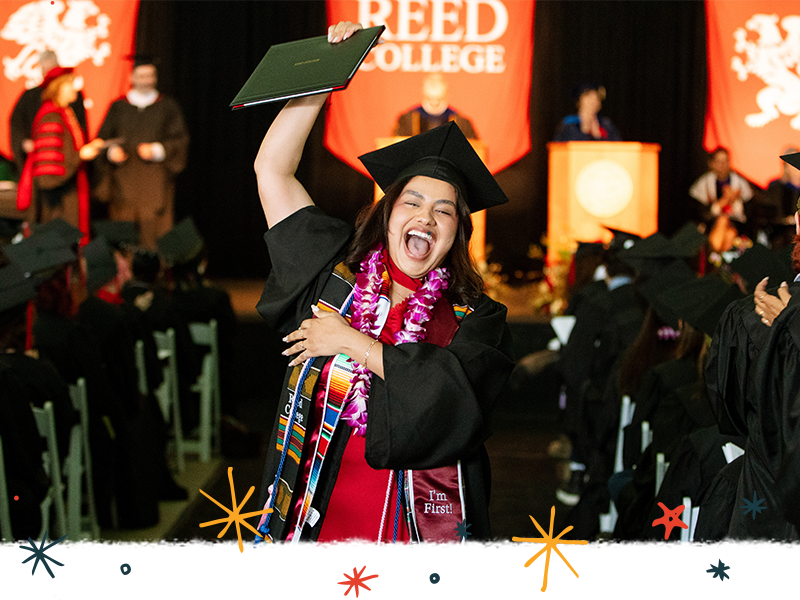 A graduate in regalia cheering with her diploma during Commencement.