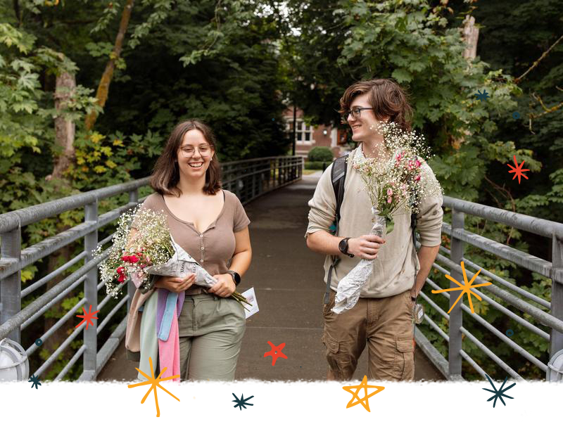 Two students walk across the blue bridge while holding flower bouquets.