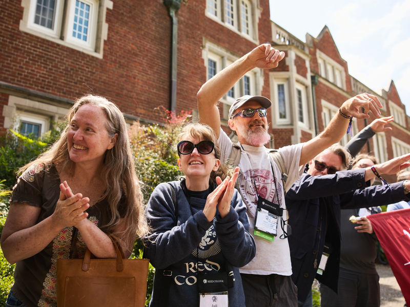 A group of alumni standing outside Old Dorm Block and cheering during Reunions.