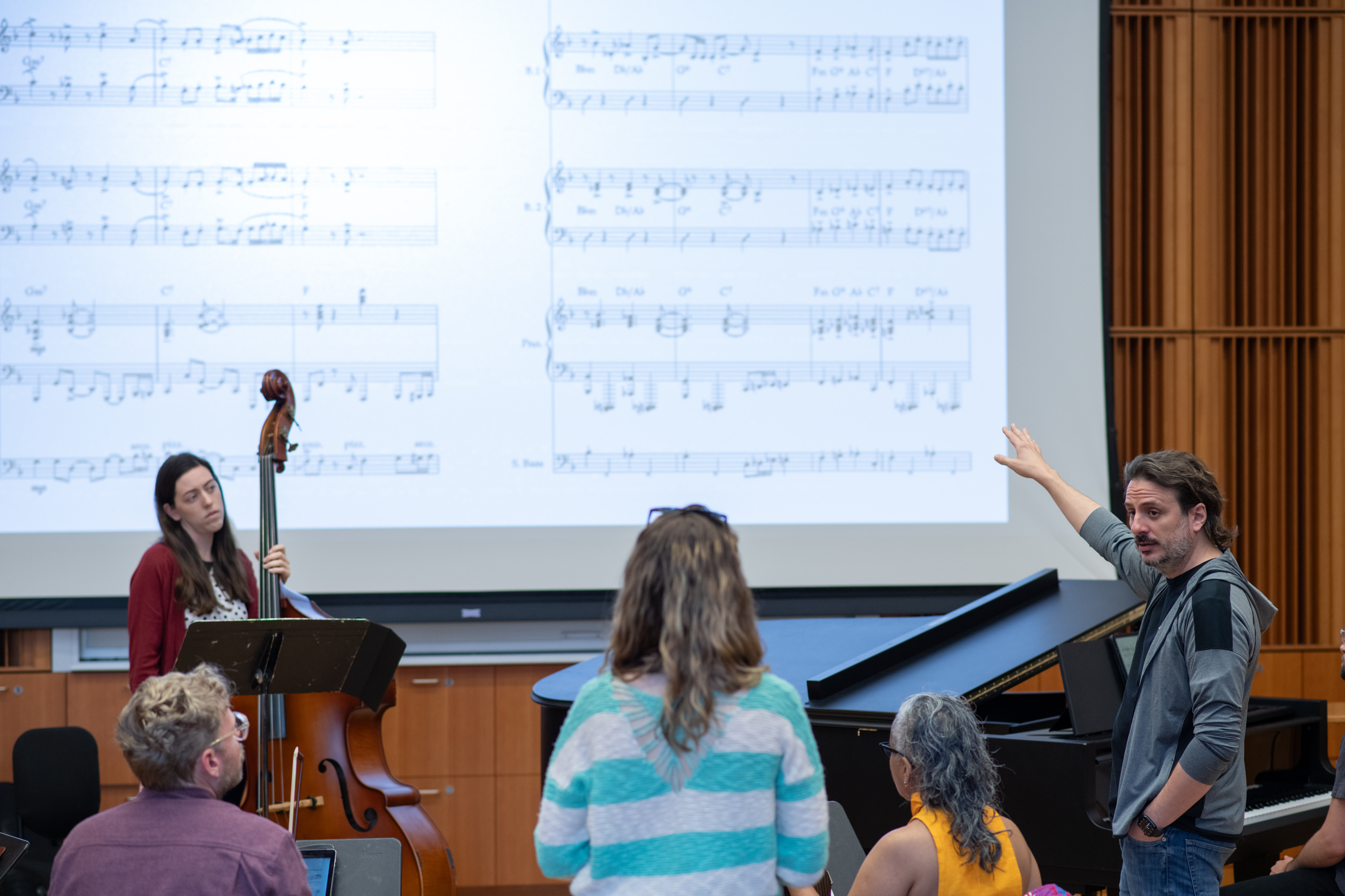 Instructor pointing at sheet music projected on screen, surrounded by students