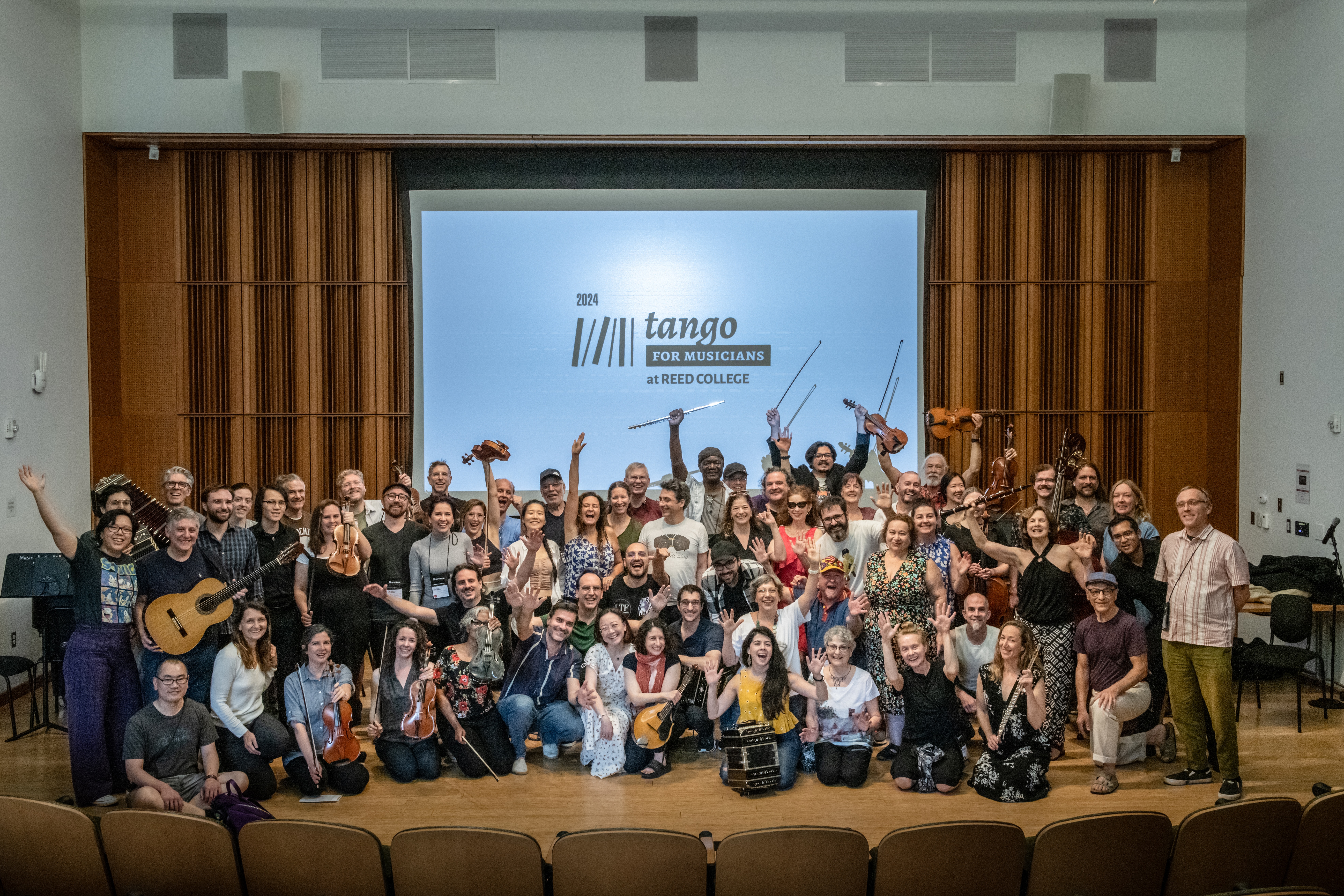 Group of several dozen people posing and smiling in front of screen that reads Tango for Musicians 2024