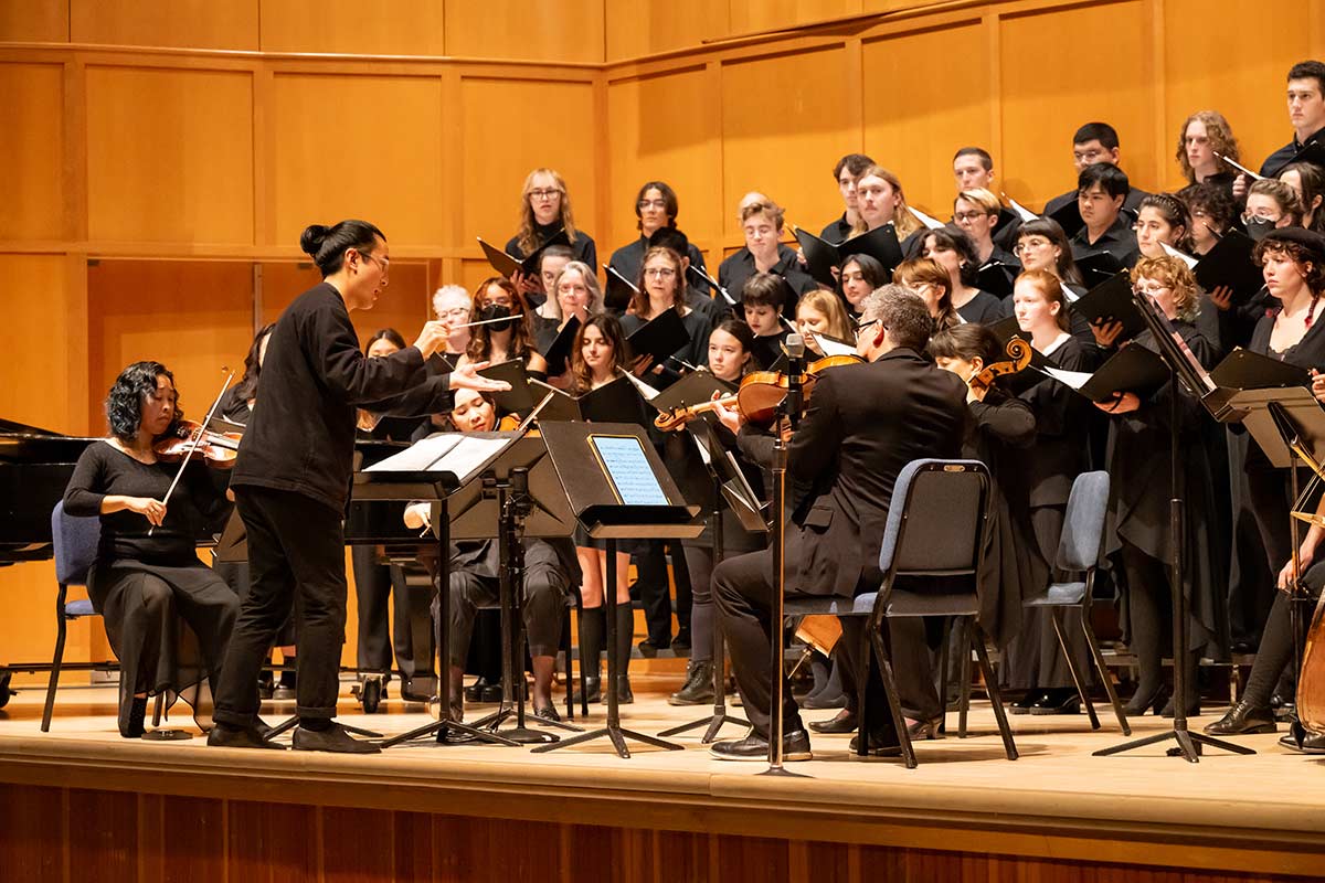 A close up view of a conductor in front of a choral ensemble