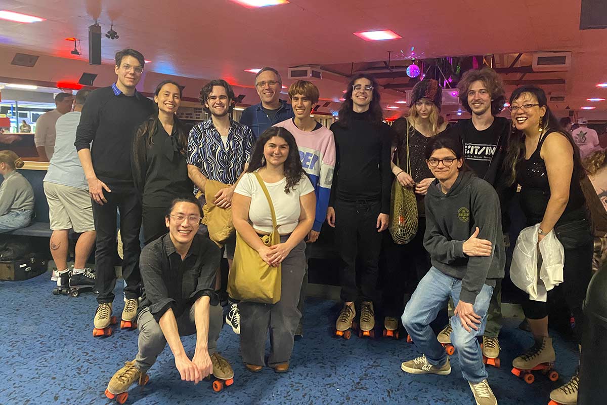 A large group of students wearing roller skates laugh and pose by a roller rink