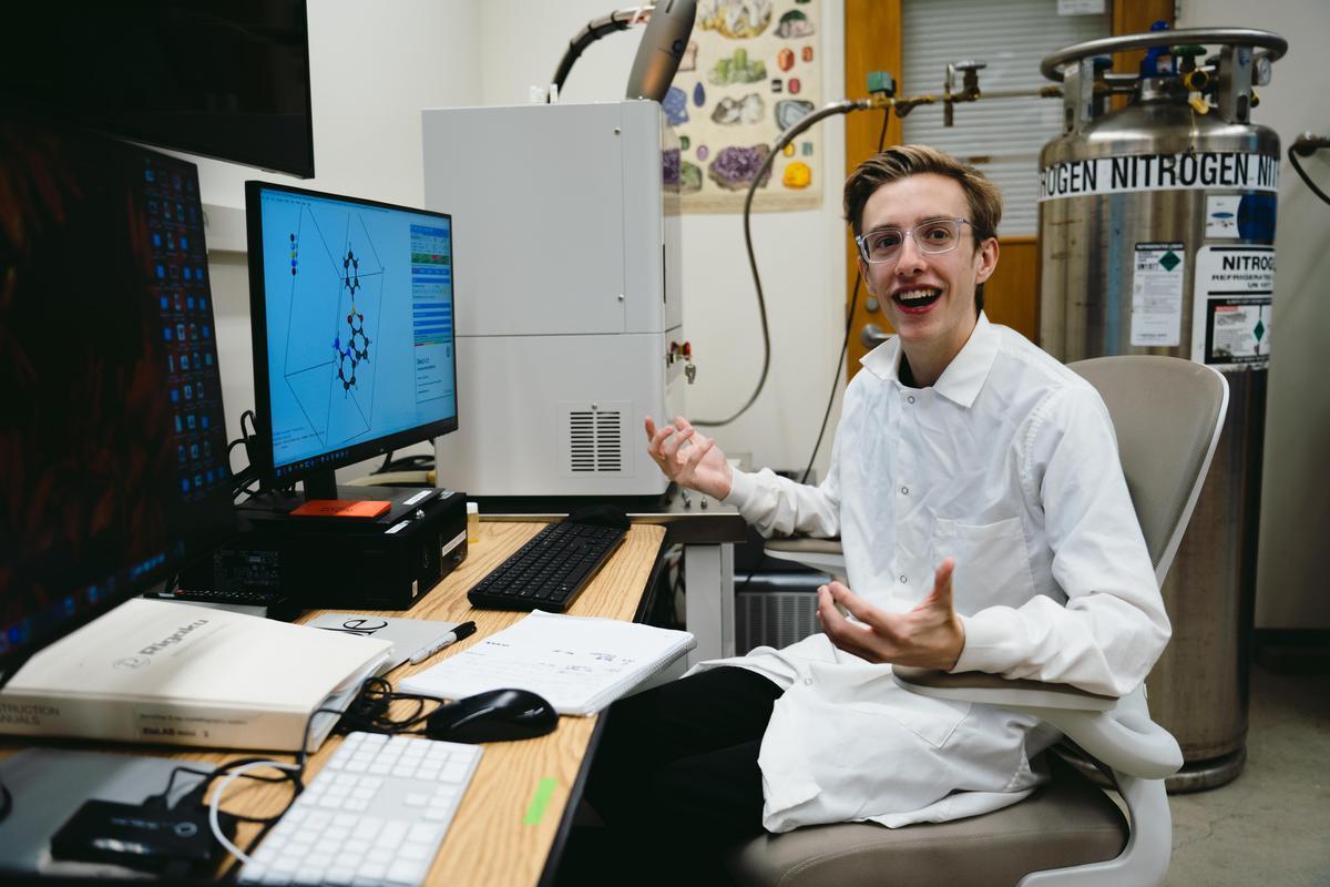 Male-presenting person in white lab coat in front of a computer