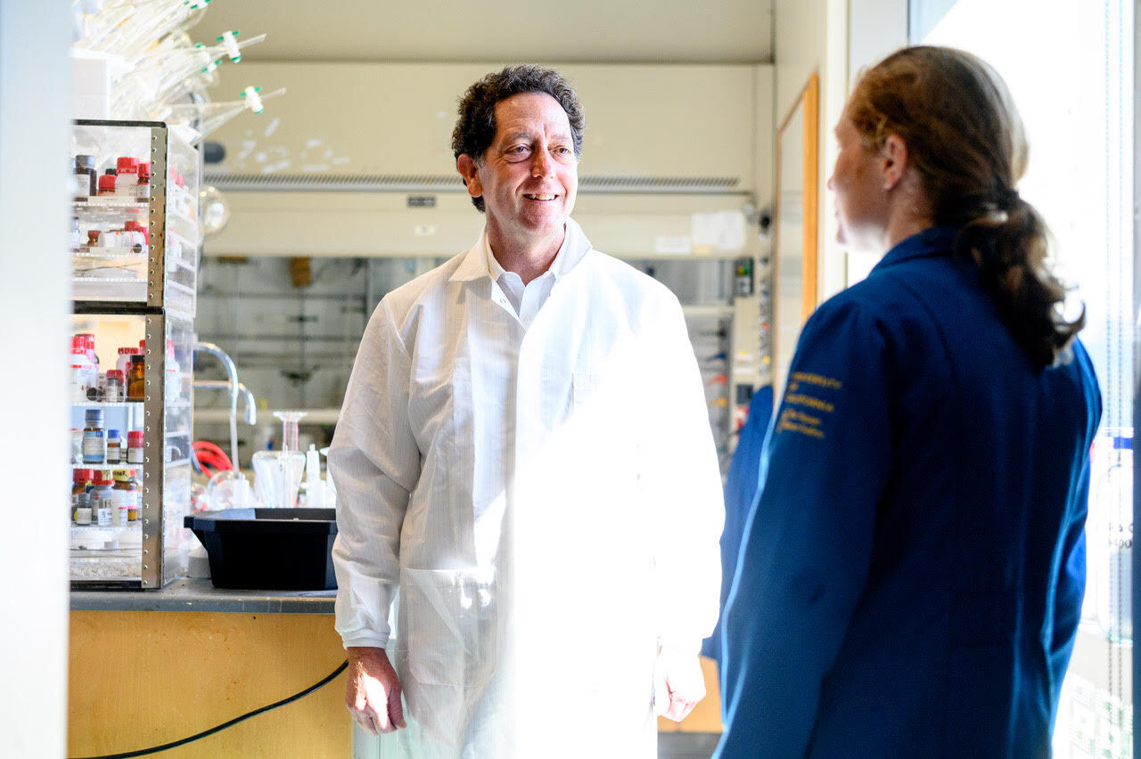 Man wearing white lab coat in a lab talking with a woman.