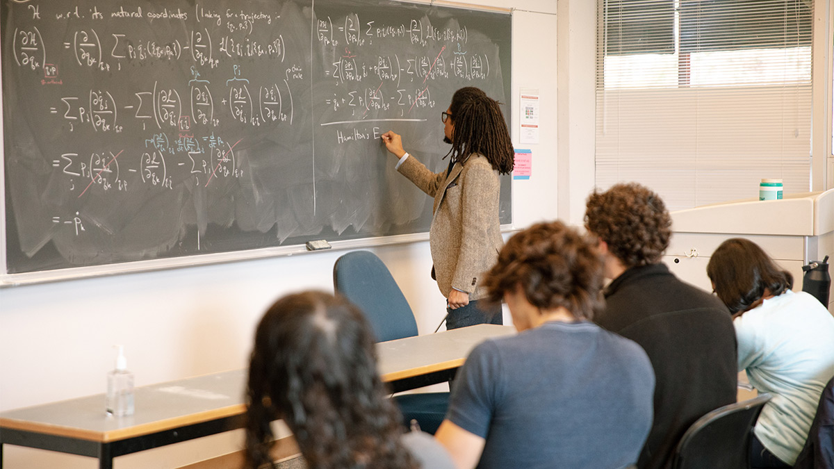 A professor writing on a chalkboard in front of a group of students. 