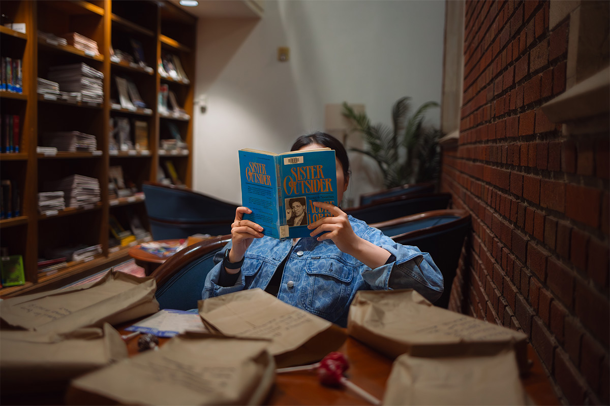 A student reads a book in the library called Sister Outsider by Audre Lorde. 
