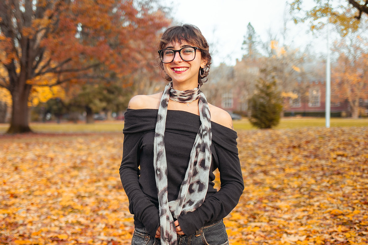 A student poses on the Great Lawn at Reed College, surrounded by fall foliage. 