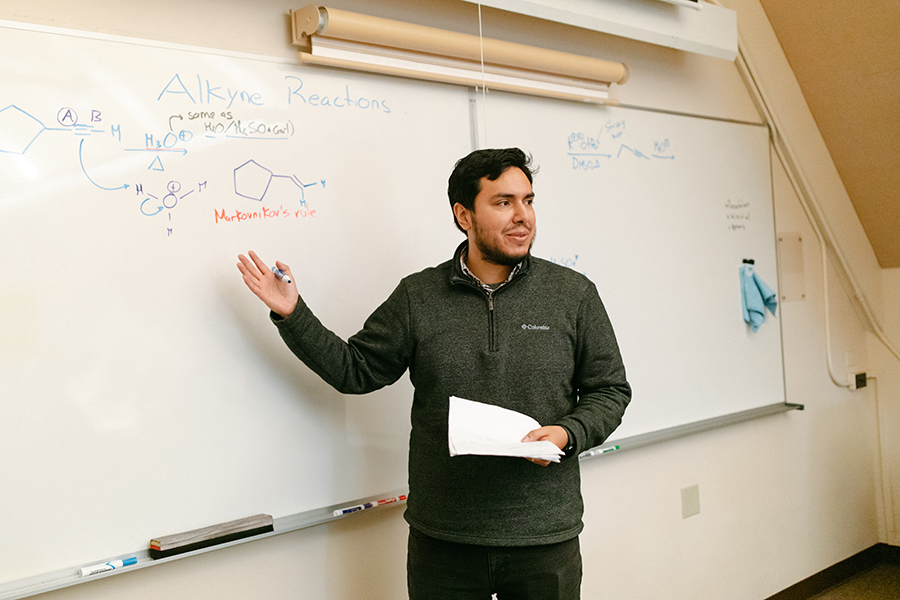 Professor Gonzalo Campillo-Alvarado standing in front of a white board with a chemical equation.