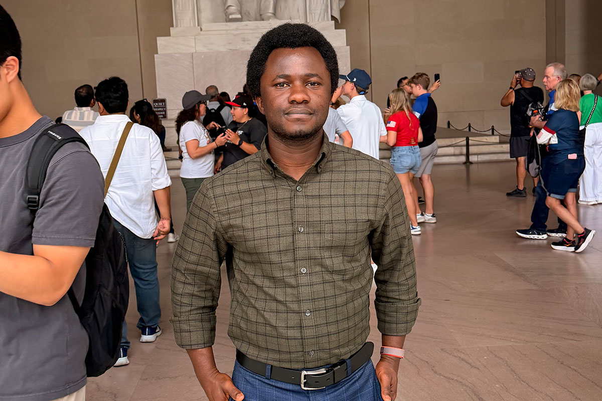 Foster Echia poses at a monument in Washington, DC, surrounded by people.