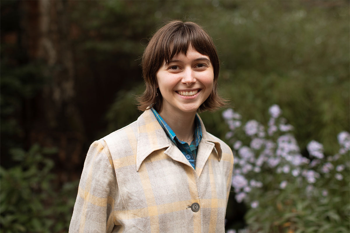 A person smiles for a headshot in front of flowers.