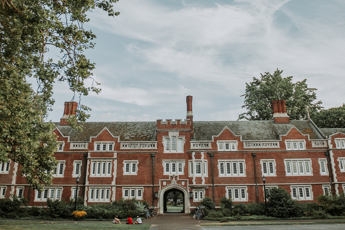 Three Reed students sitting on the grass in front of a building on campus. 