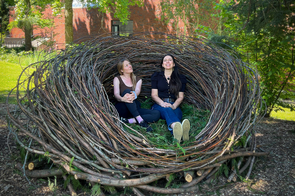 Two women sit in large nest outdoors