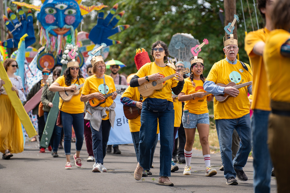 Kate and others with yellow t-shirts, ukuleles, and giant puppet