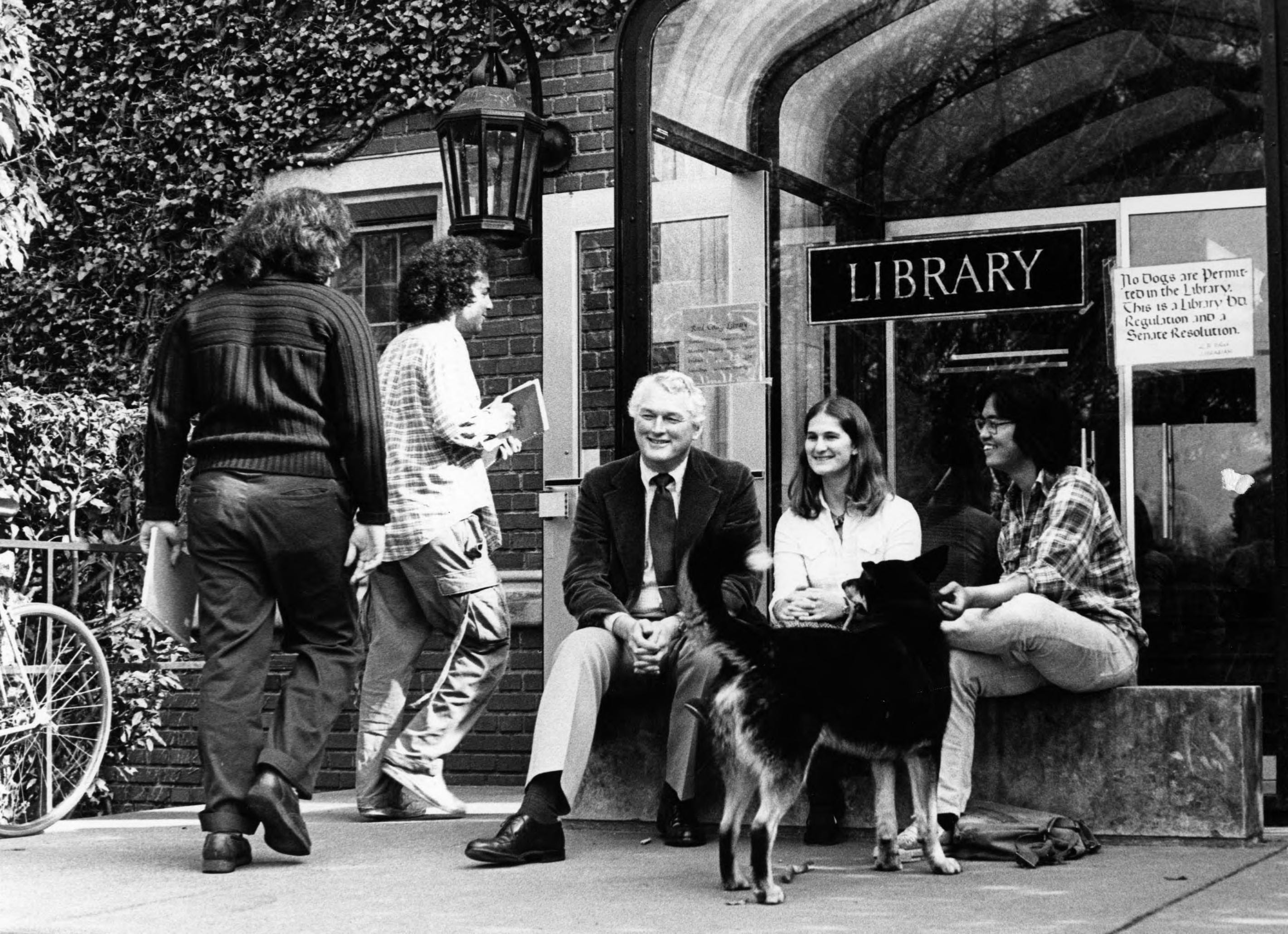 photo of former Reed President Paul Bragdon seated with two students in front of the glass-covered, original west-side entrance to the Hauser Memorial Library