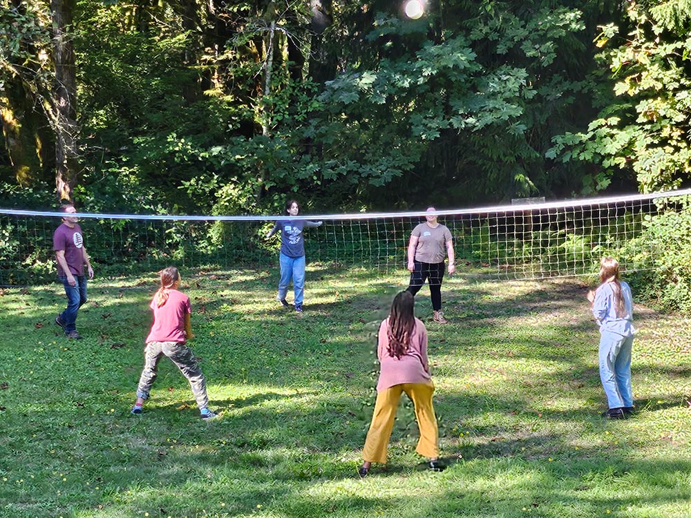 Six students playing volleyball on a grassy field