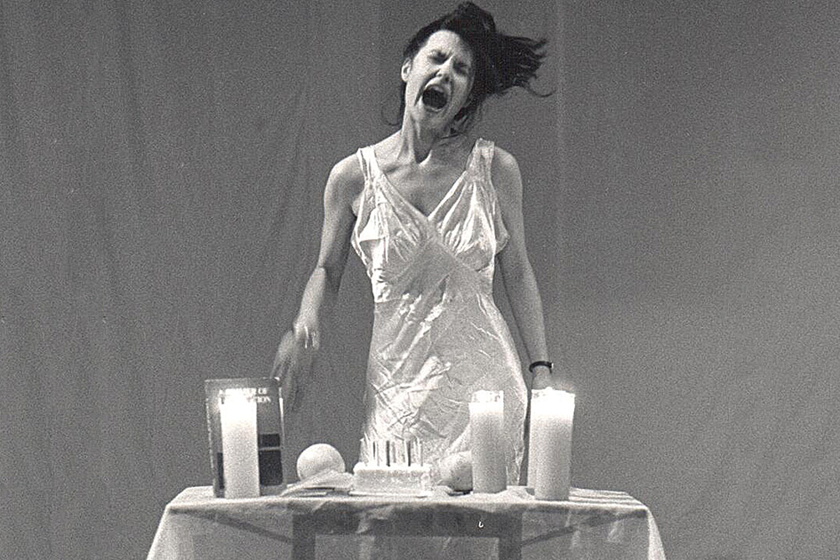Karen Finley screaming with objects on a table