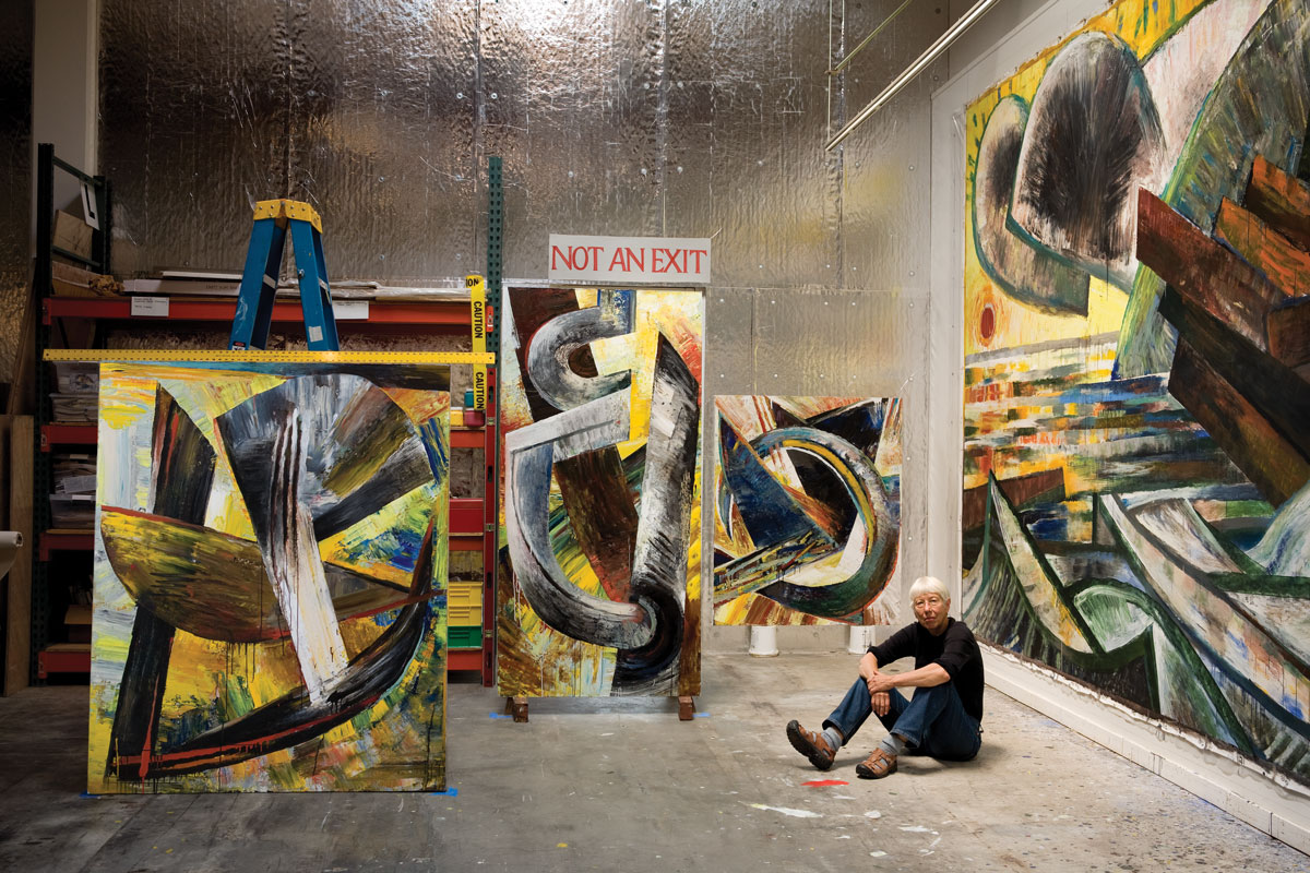 Lucinda Parker &amp;#8217;66 sits in her studio among paintings for her No Exit exhibition. The title of the show was inspired by the studio&amp;#8217;s code-required sign.