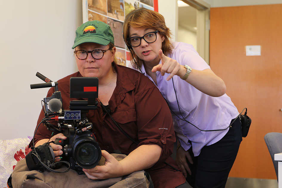 Photo of an individual holding a camera while Laura Nix leans down to talk to them