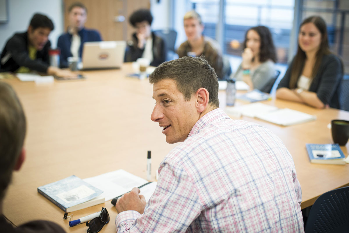 photo of professor Josh Howe at a large table with students in the classroom 