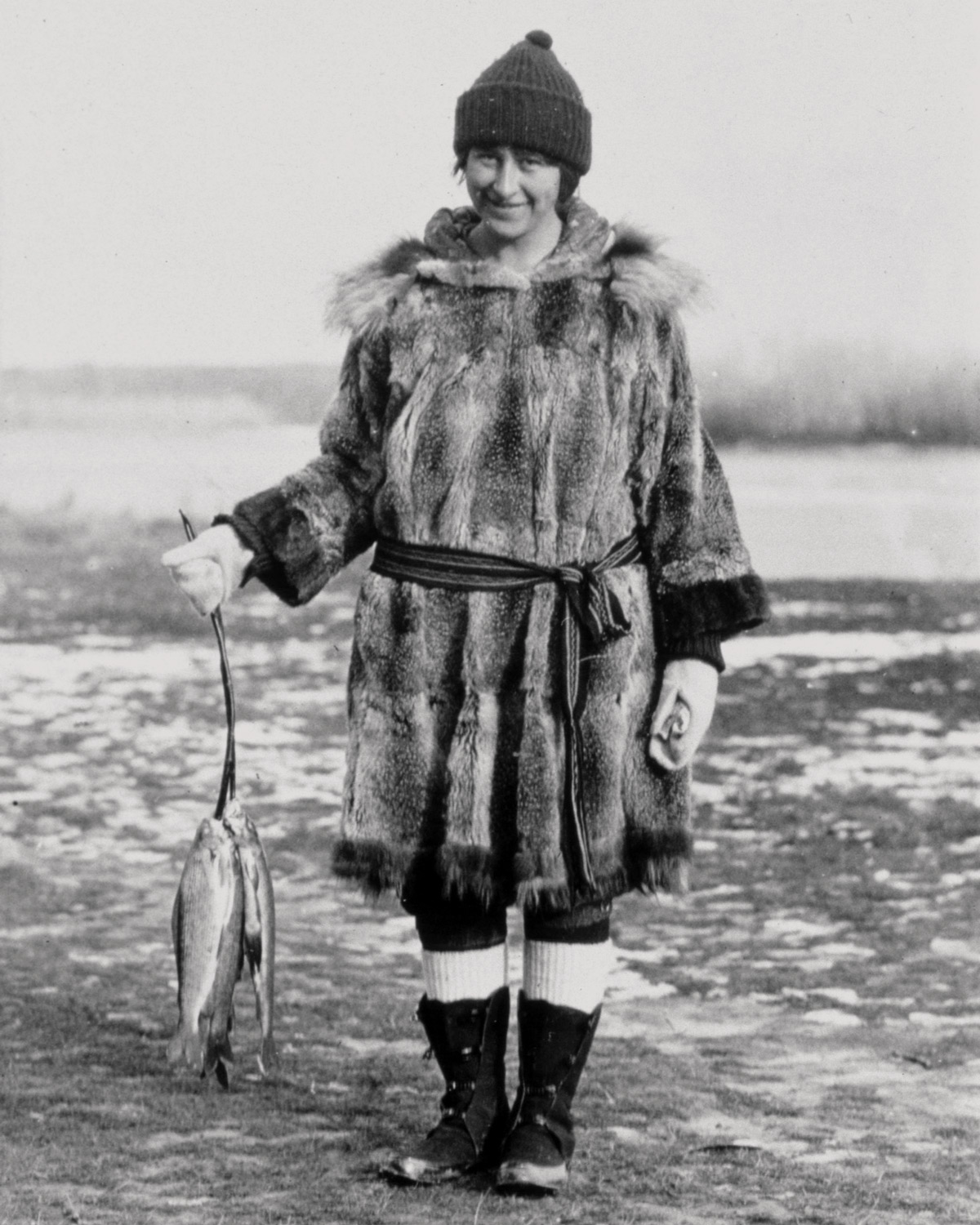 Mardy Murie in fur suit with snow and ice around with fish in hand