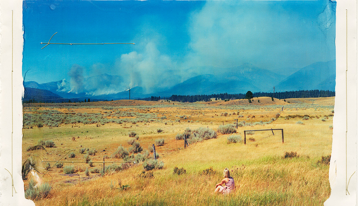 Image of woman in a pink dress in a field watching smoke in the distance.