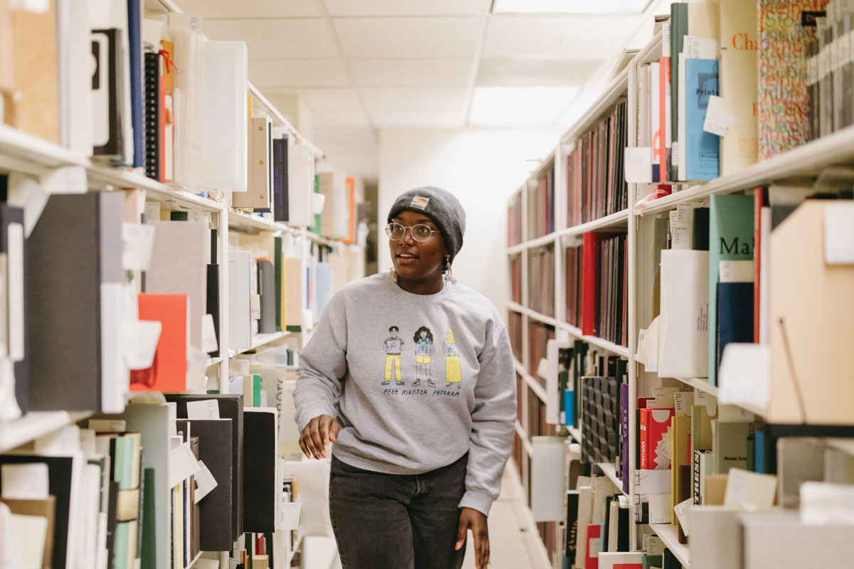 Monique Queen ’22 passes by shelves that hold student theses and artist books housed in Reed’s special collections in the Eric V. Hauser Memorial Library. 