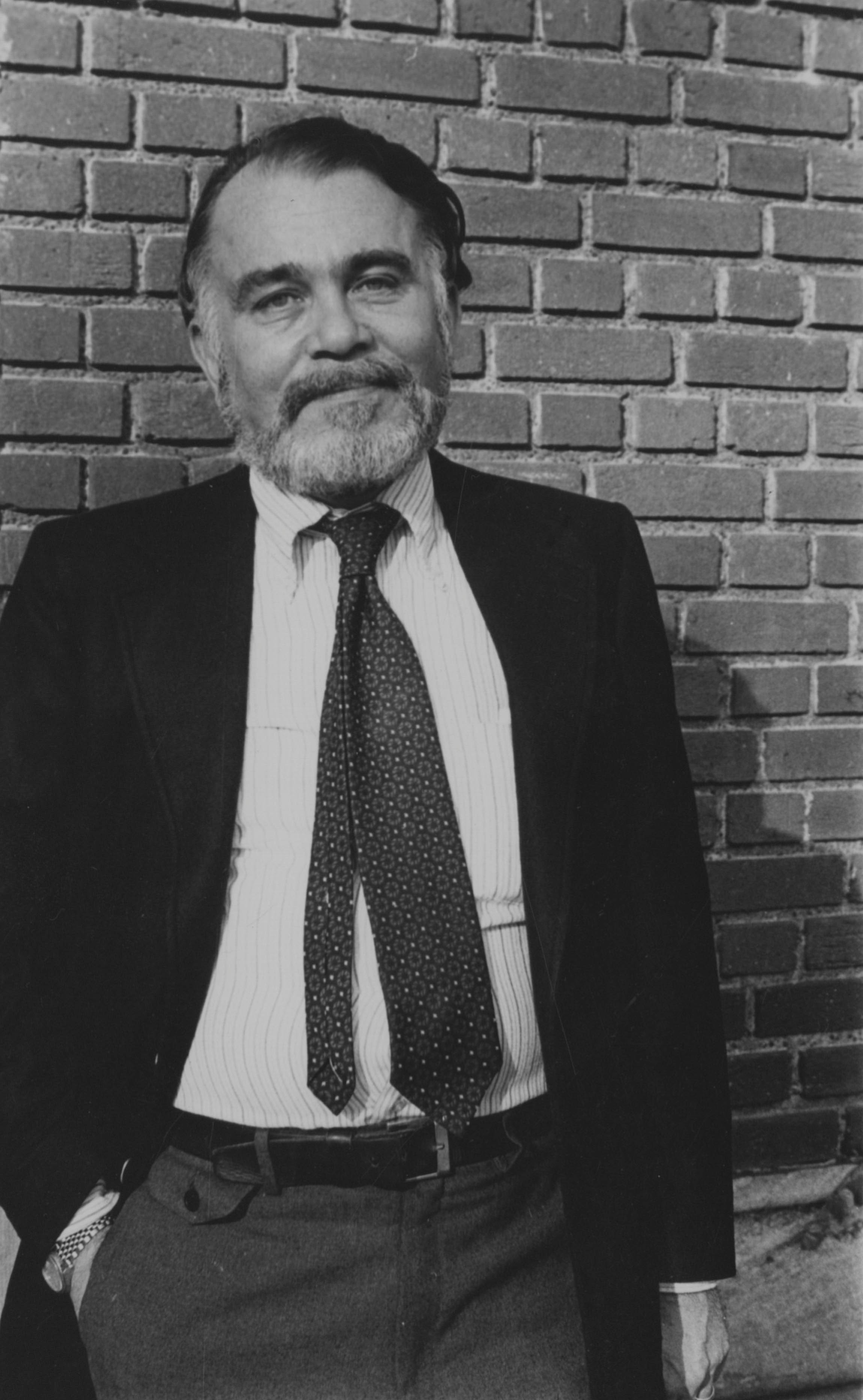 Prof. Marvin Levich in a full suit standing against a brick wall