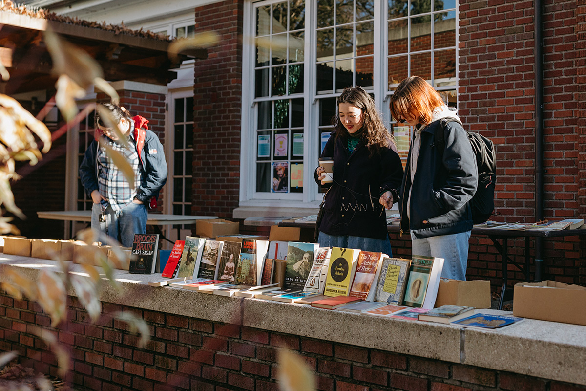 A couple of Reed students looking at books on tables outside on campus. 