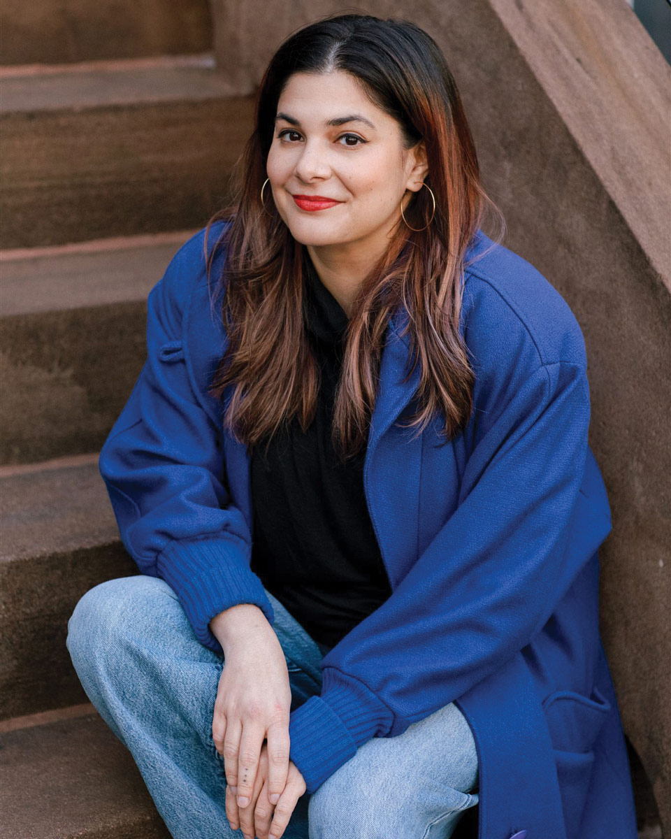 Arianna Rebolini sitting on the stairs in a blue jacket and jeans