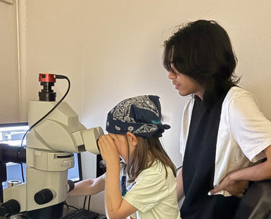 Reedie helping student observe something in a microscope.