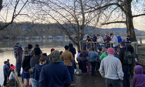 A large group of young students dressed in warm coats and hats watch salmon being released into the Willamette River