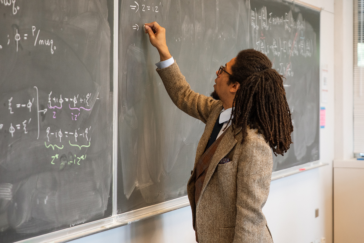 A professor writing on a chalkboard in a classroom.