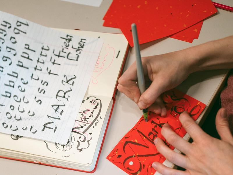 Overhead view of someone practicing calligraphy on red and white paper.