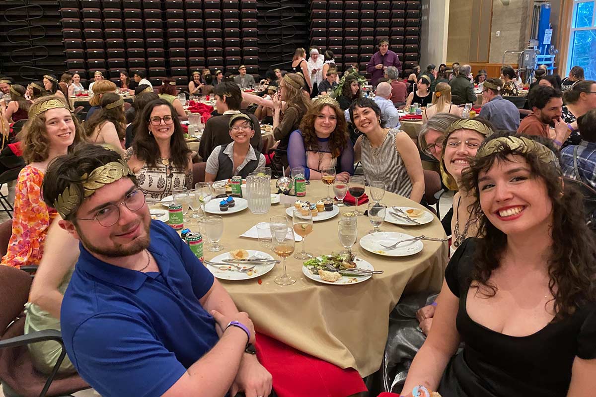 Smiling Theatre students sitting around table set for dinner with faculty