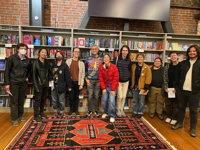 Group of students posing around adult in front of bookshelves