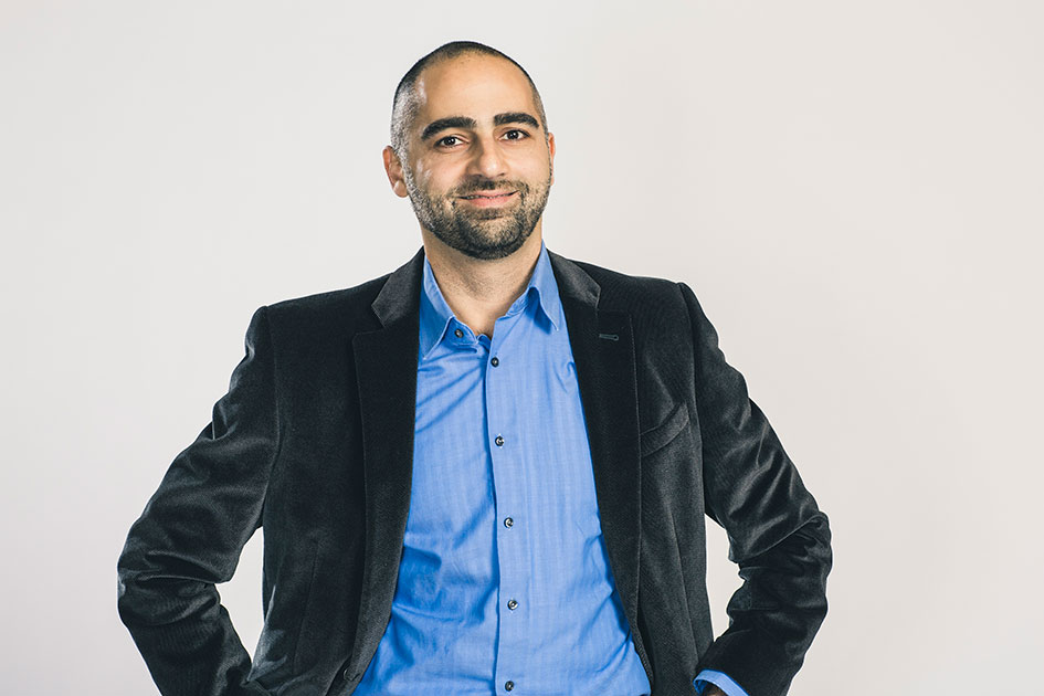 Professional headshot of a person wearing a black blazer and blue shirt.